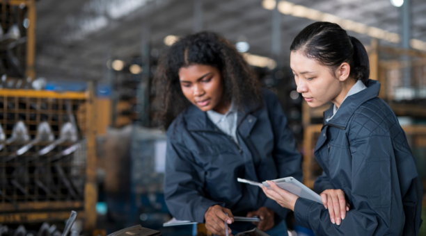 Two women wearing navy jackets looking down at a machine.