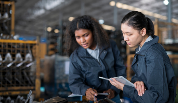 Two women wearing navy jackets looking down at a machine.