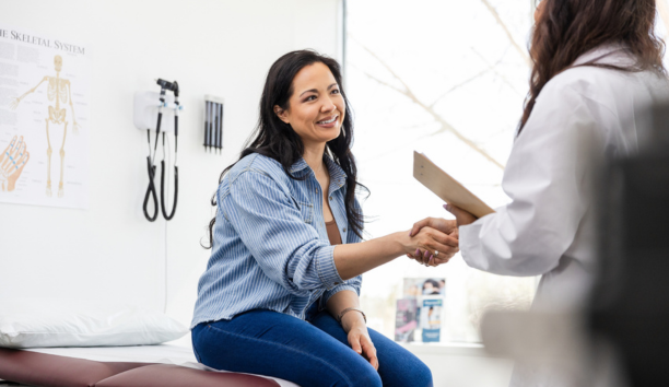 Young woman smiles and shakes hands with her doctor. 