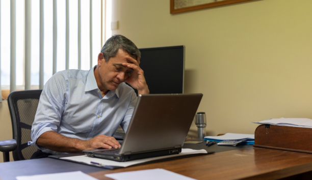 Minority man at work looking depressed while sitting at his desk on a laptop.