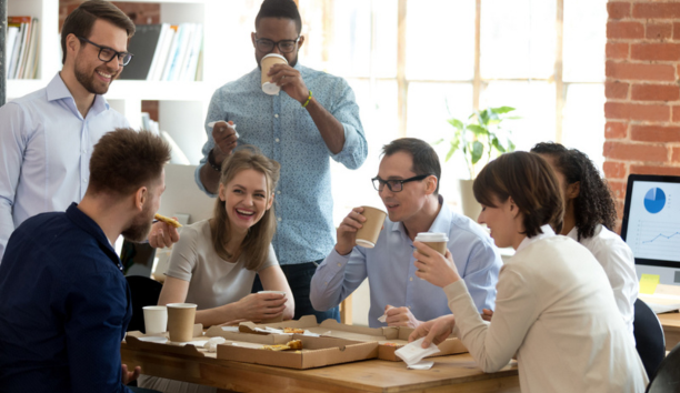 Diverse group of coworkers drinking coffee and laughing while working at a conference table. 