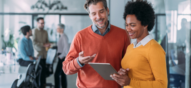 Man and woman looking at tablet in office smiling. 