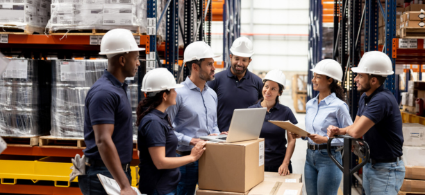 Group of employees wearing hard hats talking in a warehouse. 
