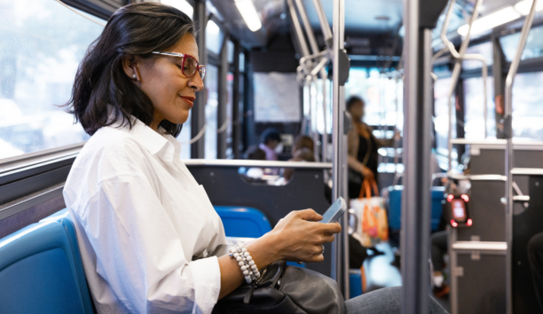 Middle aged woman commuting on a bus while looking down at her phone.
