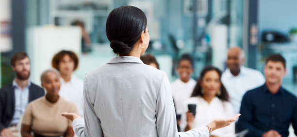 Back of woman as she speaks to a group of employees about benefits.